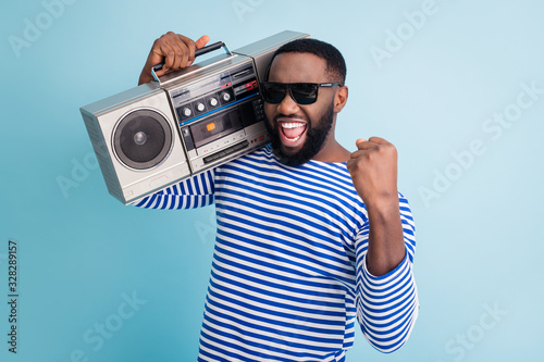 Photo of funny dark skin guy hold retro cassette recorder on shoulder raise fist amazing students party chill wear sun glasses striped sailor shirt isolated blue color background