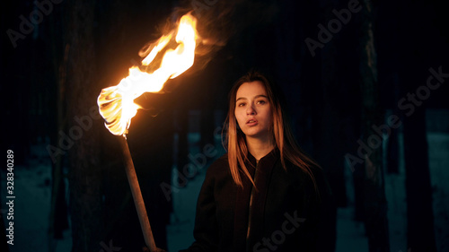 Young beautiful woman with torch in night forest