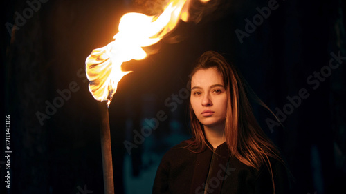 Young beautiful woman with torch in night forest looking in the camera