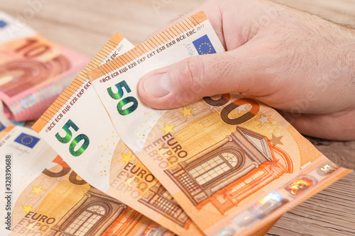 Męska dłoń trzyma dwa banknoty o nominale 50 Euro. Na drugim planie banknoty euro leżą na stole.