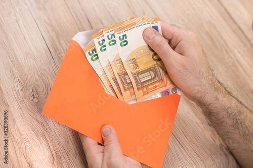 Męska dłoń trzyma kopertę i wyjmuje z niej banknoty Euro o nominałach 50 Euro.