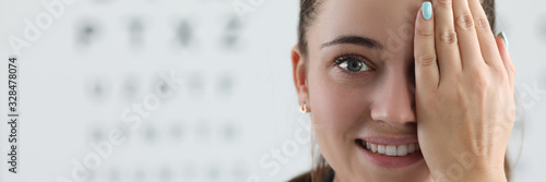 Portrait of lady oculist smiling and looking at camera with happiness. Cheerful doctor standing in clinic office and covering left eye with tender hand. Vision test concept