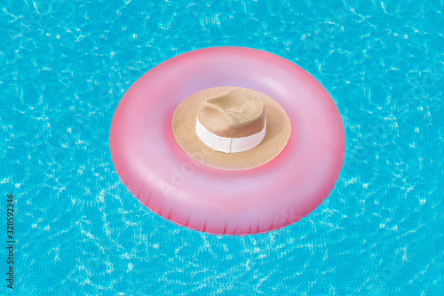A pink rubber ring on which lies a straw hat floats on the surface of the water with highlights in the pool. Vacation concept, background, summer