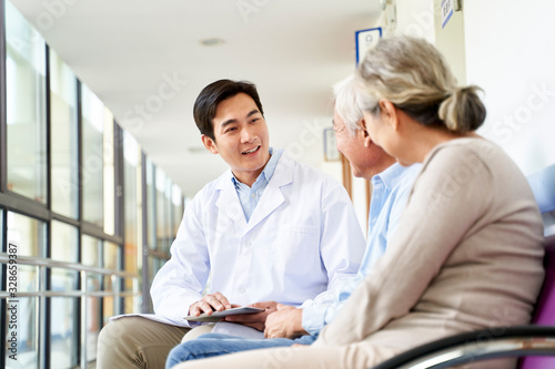 young asian doctor talking to senior couple patients in hospital hallway