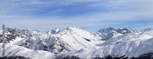Panorama of snowy slope in high winter mountains and blue sunlit cloudy sky