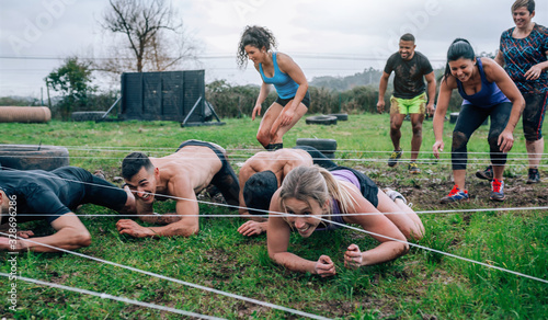 Group of participants in an obstacle course crawling under electrified cables
