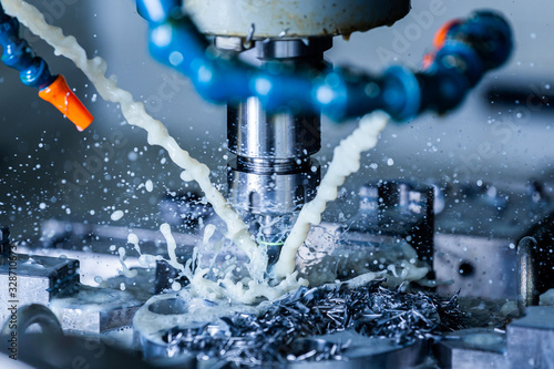 a process of vertical cnc steel milling with external water coolant streams, splashes and a lot of metal chips - close-up with selective focus