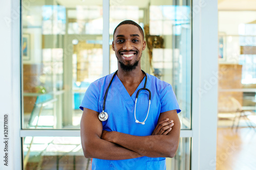 Portrait of a friendly male doctor or nurse wearing blue scrubs uniform and stethoscope, with arms crossed in hospital