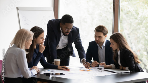 Confident african American male boss work cooperate with diverse team at office briefing, focused biracial businessman head meeting, collaborate discuss business ideas with colleagues at meeting