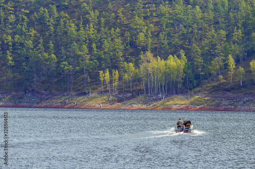 The state inspector is sailing in a motor boat along the reserved reservoir on a background of green hills