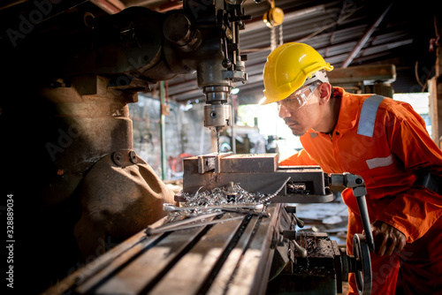 Workers in the shop wear orange work clothes and wear glasses to prevent metal chips from penetrating. Stand beside the drilling rig and use metal drills in industrial plants