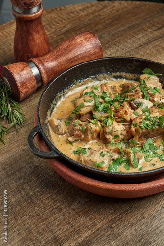 Baked potatoes with chicken in a creamy sauce in a pan on a wooden background. Close up, selective focus
