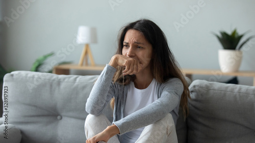 Unhappy millennial girl sit on couch in living room look in distance thinking pondering of problems, upset sad young woman lost in thoughts suffer from depression at home, psychological trauma concept