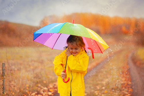 Happy girl with rainbow umbrella in autumn park