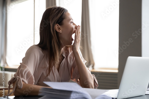 Head shot distracted from work study young woman yawning, having lack of energy during workday at home or office. Tired businesswoman feeling bored, looking at window, chronic fatigue concept.