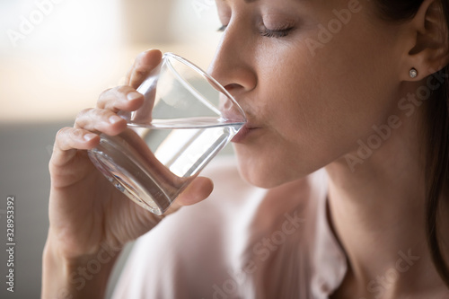 Side view head shot close up young woman drinking pure still water in morning. Healthy thirsty lady enjoying healthy lifestyle daily habit, natural beauty, perfect skin body care aqua balance concept.