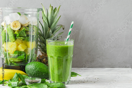 Blender with fresh ingredients to making healthy detox smoothie with glass of green prepared drink with a straw