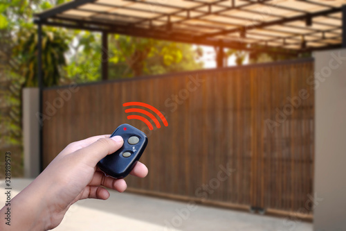 Closeup hand holding and using remote control to open or close the automatic wooden gate with home blurred background. Home remote control concept. concept.