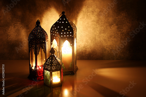 Ornamental Arabic lanterns with burning candles on table glowing at night. Festive greeting card, invitation for Muslim holy month Ramadan Kareem. Iftar dinner background with golden glow.