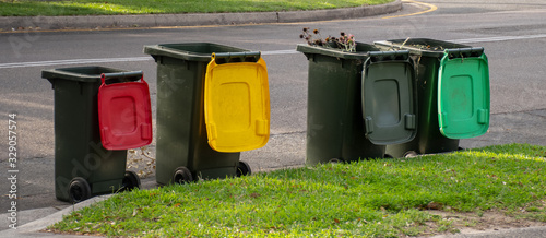 Australian garbage wheelie bins with colourful lids for recycling household waste and green garden waste lined up on the street kerbside for council rubbish collection