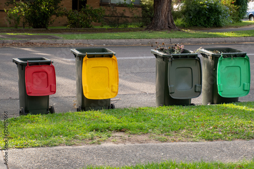 Australian garbage wheelie bins with colourful lids for recycling household waste and green garden waste lined up on the street kerbside for council rubbish collection