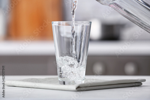 Pouring of fresh water into glass on table in kitchen