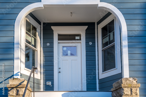 Interesting covered porch with inward windows Hardwood white front door in the entryway white frame on a blue horizontal vinyl siding newly restored American home