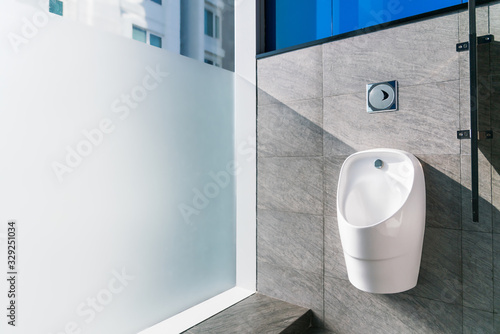 Sanitation white ceramic urinal in the men's bathroom with hygienic automatic water-saving electronic flusher. Urine sensor urinal Inductive toilet flush. Office or public bathroom. Real photo.