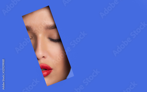Beautiful woman with red lips peeping out torn paper