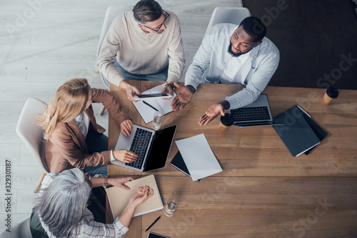 overhead view of multicultural colleagues talking and sitting at table during meeting