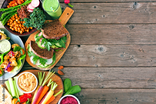 Healthy lunch food side border. Table scene with nutritious hearty bowl, sandwiches, lettuce wraps and vegetables. Top view over a rustic wood background. Copy space.