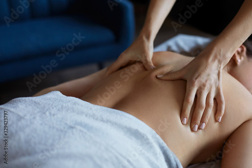 Young beautiful woman enjoying back and shouders massage in spa.Professional massage therapist is treating a female patient in apartment.Relaxation,beauty,body and face treatment concept.Home massage.