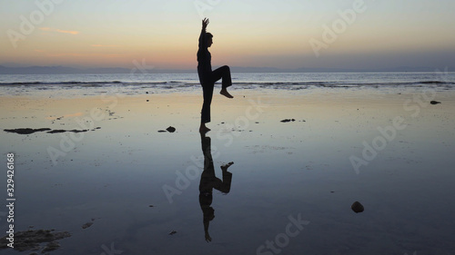 Silhouette of man practiceing qigong exercises at sunset by the sea
