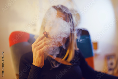 Caucasian unknown mature woman in black hold cigarillo at home while sitting in a colorful chair in the evening smoke smoking tobacco cigar