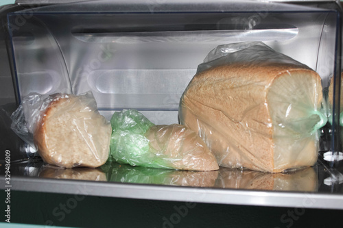 Different loaves of bread in a bread box and cellophane bags.