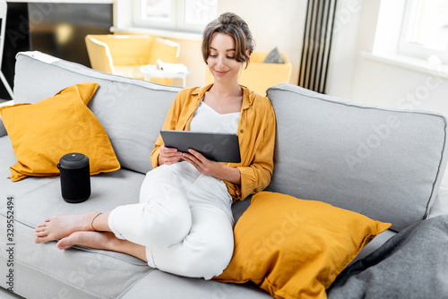 Young and cheerful woman using a digital tablet while sitting relaxed on the couch at home. Concept of a leisure activities with mobile devices at home