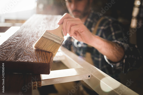 Close up of paintbrush applies paint or varnish on wooden board in carpentry workshop