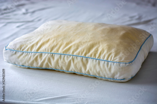 Old dirty used yellow sweat stained pillow on a mattress. Condition of the pillow used for a long time.