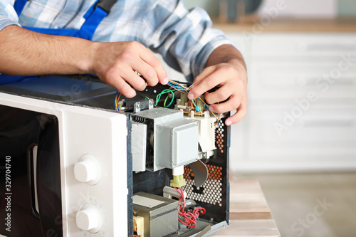 Worker repairing microwave oven in kitchen, closeup