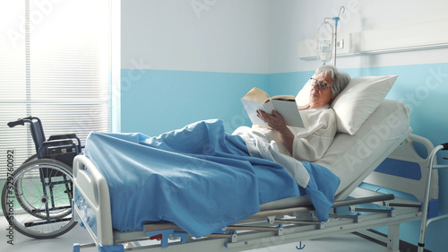 Senior woman lying in bed at the hospital and reading