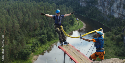 Young man jumping with a rope from a great height into the deep canyon on the background of the forest and river below, panorama. Ropejumping.