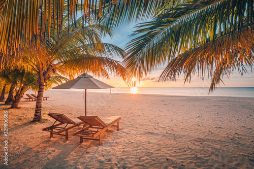 Beautiful tropical sunset scenery, two sun beds, loungers, umbrella under palm tree. White sand, sea view with horizon, colorful twilight sky, calmness and relaxation. Inspirational beach resort hotel