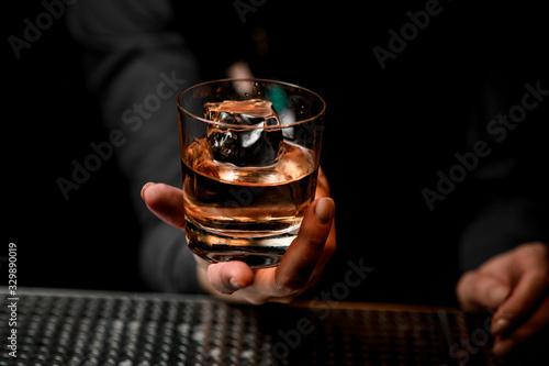 close-up of glass with alcoholic drink in bartender's hand.