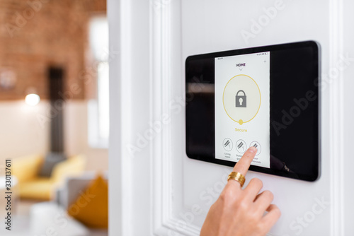 Controlling home alarm system with a digital touch screen panel installed on the wall. Concept of wireless secure control and smart home