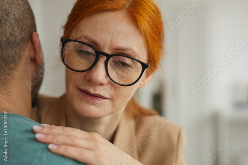 Close-up of red haired woman in eyeglasses embracing the man while they standing in the room