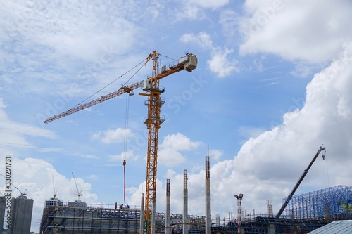 Looking up of tower crane on sky and cloud with sun shining as a background in the construction site, Space for text in template, Industrial skyline