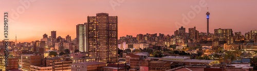 A beautiful and dramatic panoramic photograph of the Johannesburg city skyline, taken on a golden evening after sunset.