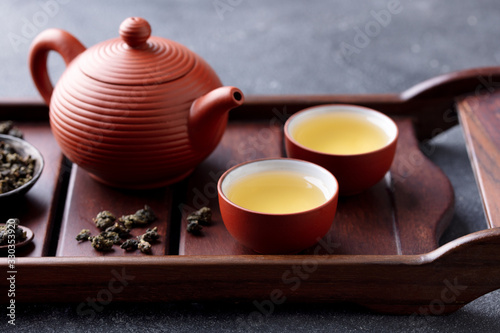 Green tea oolong in teapot and chawan bowls, cups on a wooden tray. Grey background. Close up.