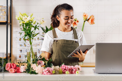 Smiling florist woman holding a digital tablet while standing at the counter in her shop