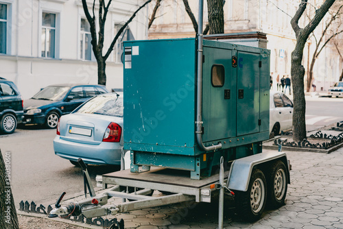 Mobile moveable gensets portable diesel engine power electric generator on a trailer stands on the city's street. Green. Urban. Electricity. Power supplier for business. Outdoor. Sidewalk. Road. Wheel